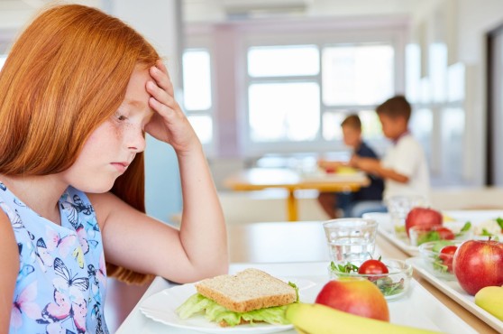 Nena trista davant d'un plat en un menjador escolar